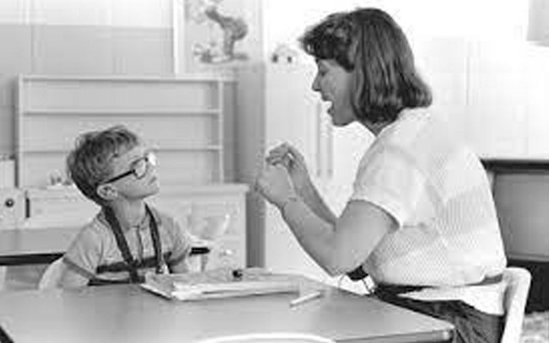 Film still from DEAF. A teacher and a child are sitting at a table in the classroom.