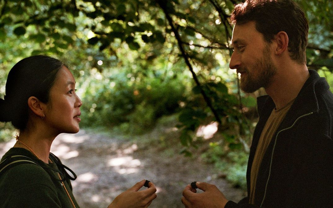 Filmstill aus HERE: Zwei Menschen schauen sich an, sie stehen in einem Wald.