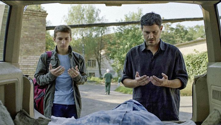 Filmstill aus HOMEWARD: Ein Vater und sein Sohn stehen vor dem offenen Kofferraum ihres Autos und sprechen ein Gebet.