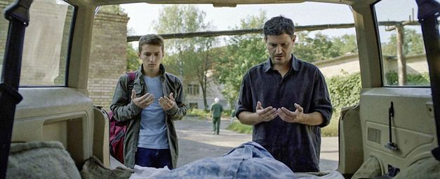 Filmstill aus HOMEWARD: Ein Vater und sein Sohn stehen vor dem offenen Kofferraum ihres Autos und sprechen ein Gebet.