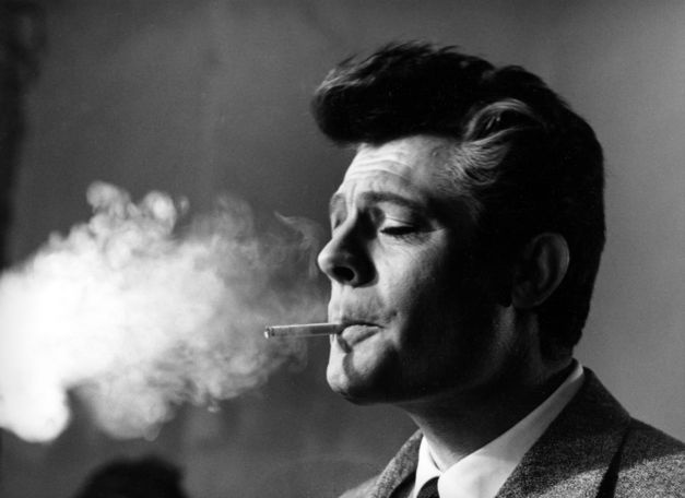 Black and white photograph of Marcello Mastroianni smoking a cigarette. The smoke fills the left part of the photo.