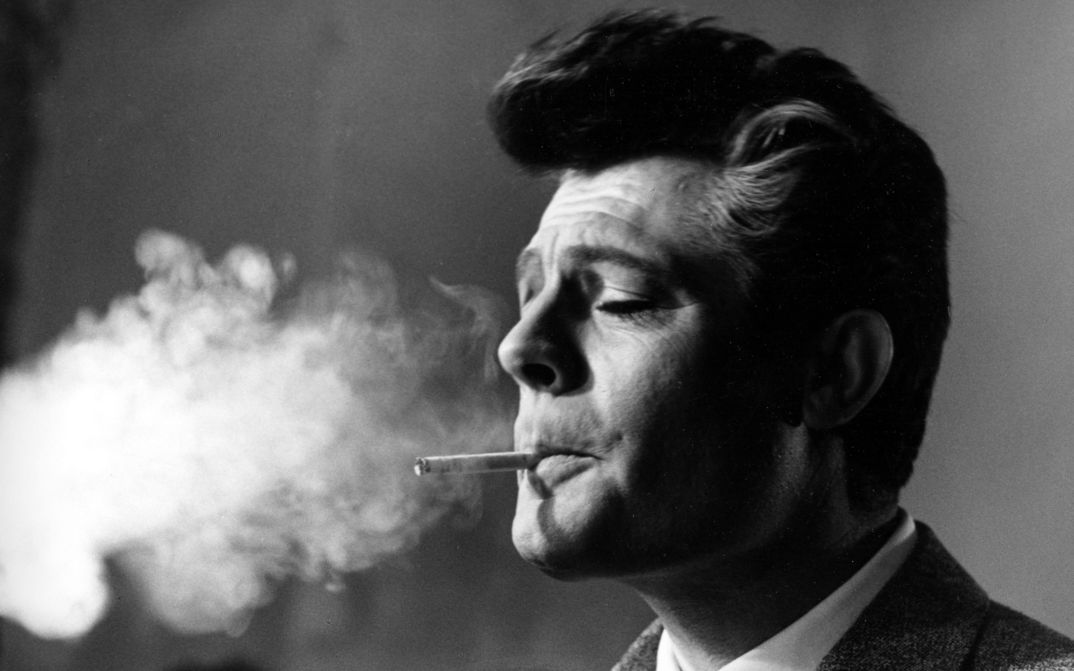 Schwarz-Weiß-Fotografie von Marcello Mastroianni, der eine Zigarette raucht. Der Rauch füllt den linken Teil des Fotos.