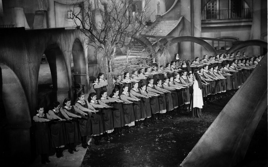 Filmstill aus MUCHACHAS DE UNIFORME: In einem expressionistischen Setting stehen aufgereiht Schulmädchen in Uniform. Eine Nonne inspiziert ihre ausgestreckten Hände.
