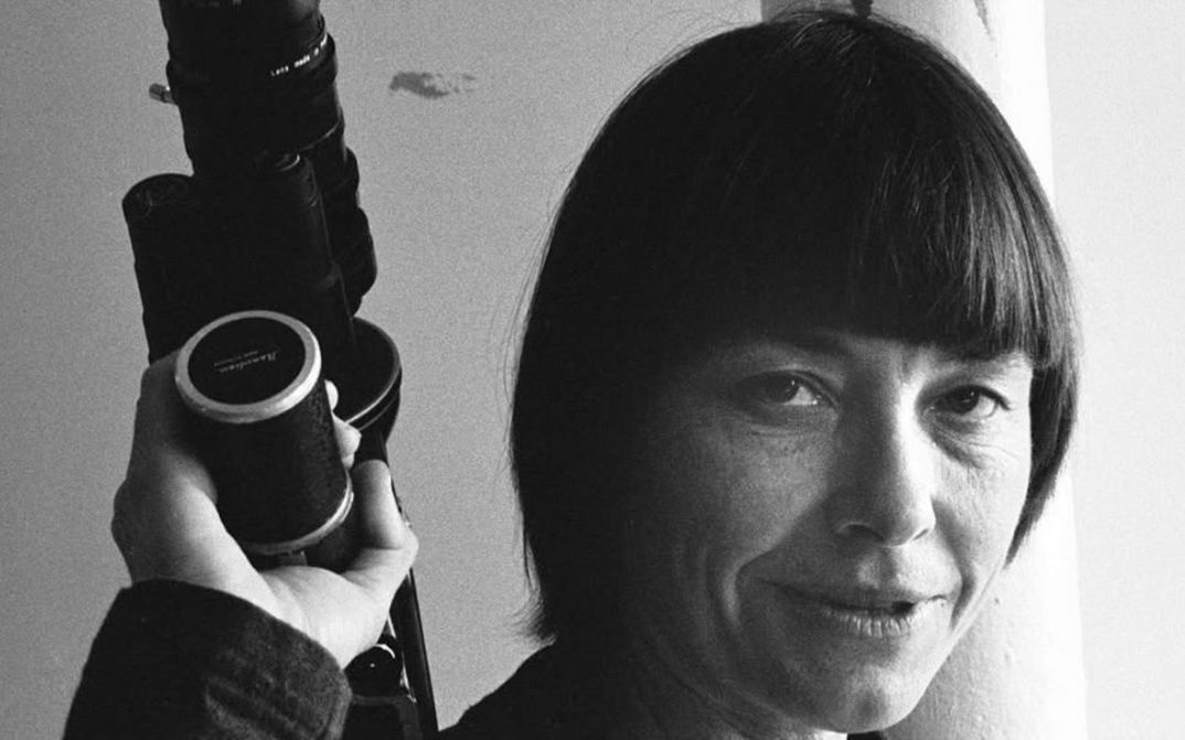 Schwarzweißporträt einer Frau mit Kurzhaarschnitt, die eine Kamera oder ein Objektiv in der Hand hält.