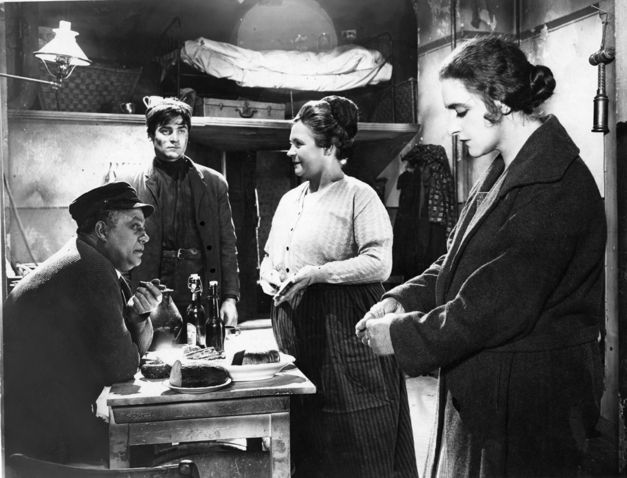Film still from ZUFLUCHT. Four people are standing around a small table.