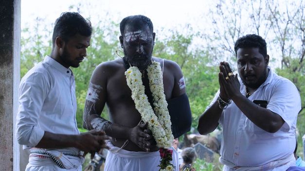 Drei Männer führen religiöses Ritual durch, Blumenkranz und Gebetshaltung.