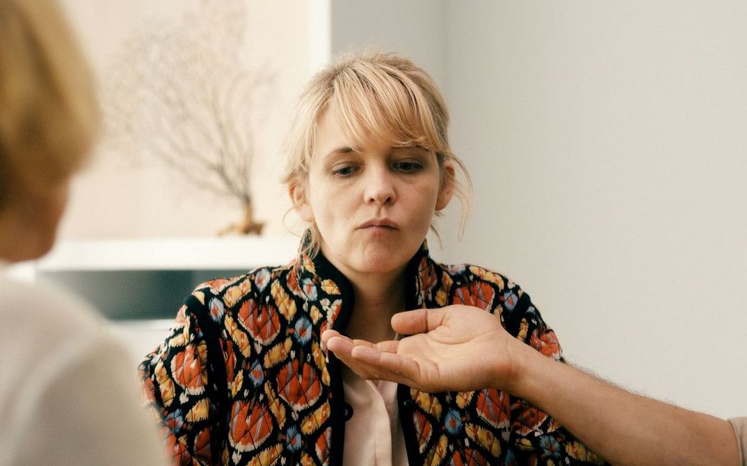 Filmstill aus HEDI SCHNEIDER STECKT FEST: Man sieht eine blonde Frau, die im Begriff ist, etwas auszuspucken. Jemand hält eine Hand vor ihren Mund.