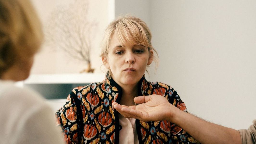 Filmstill aus HEDI SCHNEIDER STECKT FEST: Man sieht eine blonde Frau, die im Begriff ist, etwas auszuspucken. Jemand hält eine Hand vor ihren Mund.