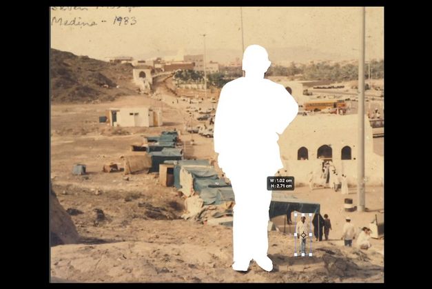 Film still from Abdul Halik Azeez’s „Desert Dreaming“. A view from a hill on the outskirts of an arid town. In the center of the picture a person is cut out and pasted on its right in a shrunken version.