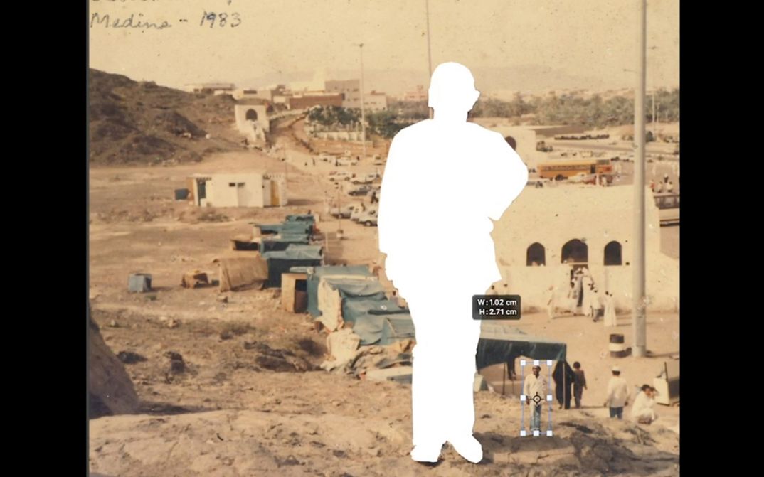 Film still from Abdul Halik Azeez’s „Desert Dreaming“. A view from a hill on the outskirts of an arid town. In the center of the picture a person is cut out and pasted on its right in a shrunken version.
