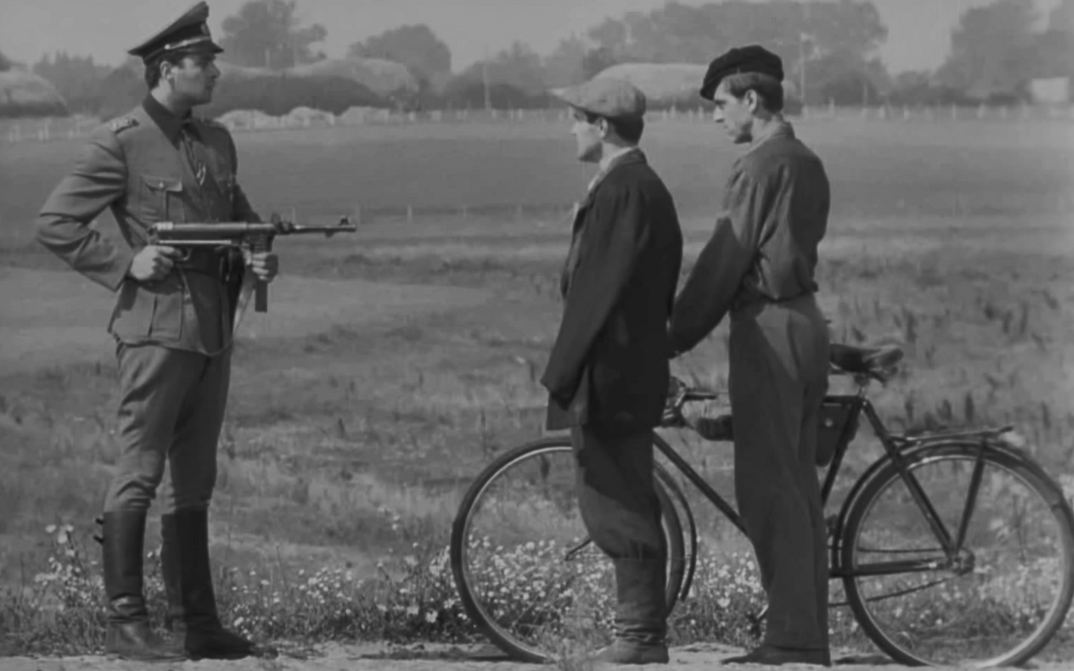 Film still from SOVIST: A soldier holds a rifle on two men with a bicycle.