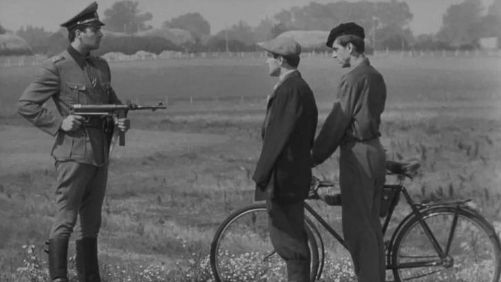 Filmstill aus SOVIST: Ein Soldat hält ein Gewehr auf zwei Männer mit einem Fahrrad.
