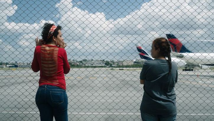 Filmstill aus O ESTRANHO: Zwei Frauen blicken durch einen Maschendrahtzaun auf ein Flugfeld.