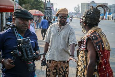 Three people on a film set, one with camera, one in disguise