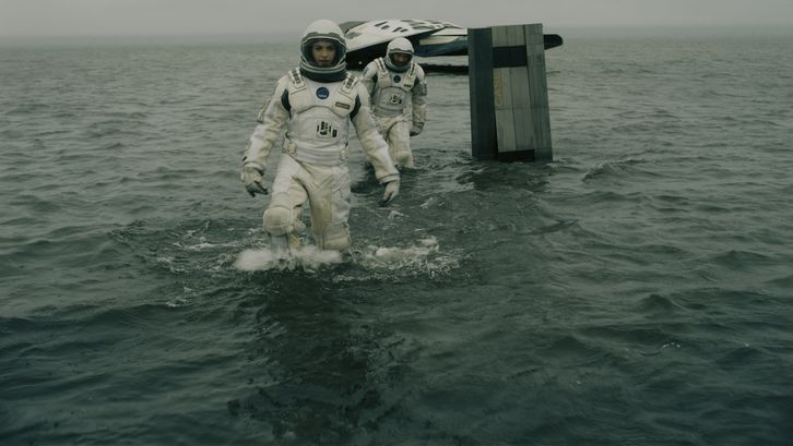 Filmstill aus INTERSTELLAR: Zwei Astronaut*innen bewegen sich in Raumanzügen im Wasser, im Hintergrund sieht man ein kleines Raumschiff.