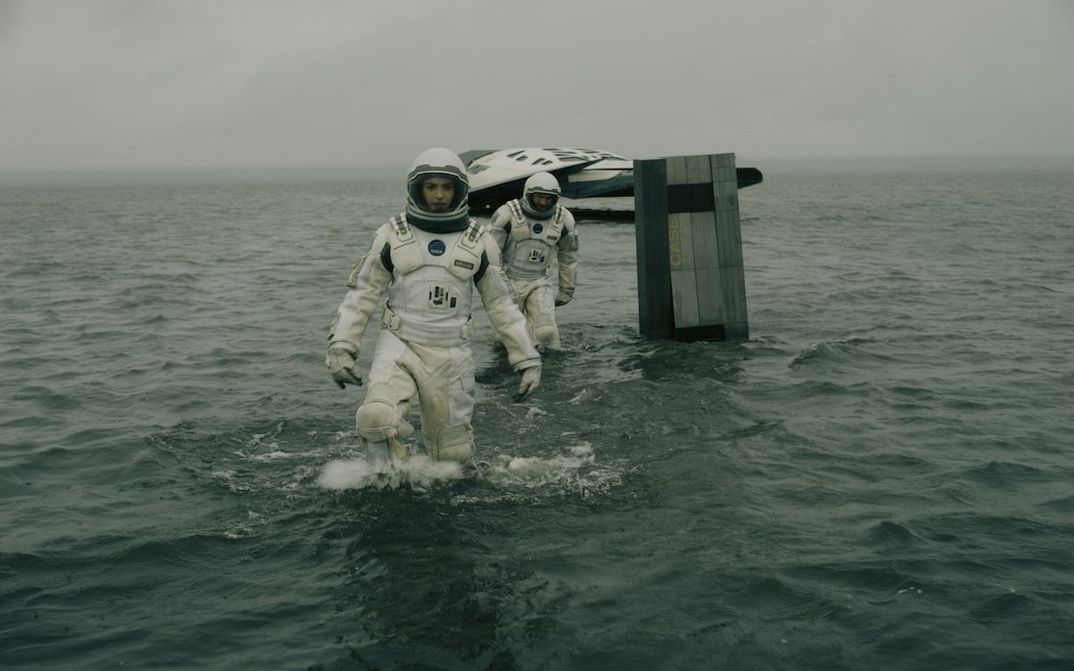 Filmstill aus INTERSTELLAR: Zwei Astronaut*innen bewegen sich in Raumanzügen im Wasser, im Hintergrund sieht man ein kleines Raumschiff.