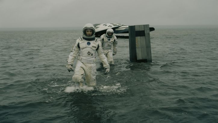Film still from INTERSTELLAR: Two astronauts in space suits are moving in the water, in the background you can see a small spaceship.