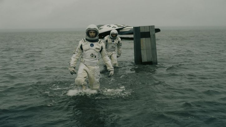 Film still from INTERSTELLAR: Two astronauts in space suits are moving in the water, in the background you can see a small spaceship.