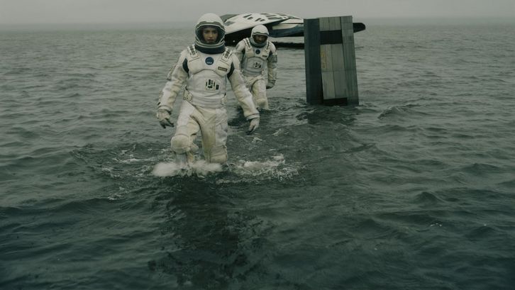 Filmstill aus INTERSTELLAR: Zwei Astronaut*innen bewegen sich in Raumanzügen im Wasser, im Hintergrund sieht man ein kleines Raumschiff.
