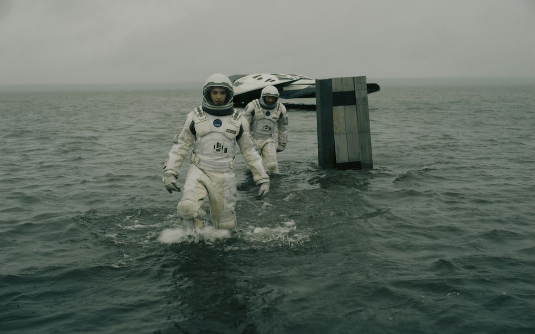 Filmstill aus INTERSTELLAR: Zwei Astronaut*innen bewegen sich in Raumanzügen im Wasser, im Hintergrund sieht man ein kleines Raumschiff.