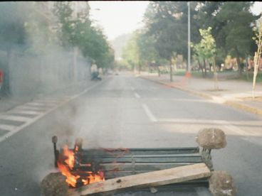 35-mm-Farbfoto einer umgestürzten, brennenden Bank mitten auf der Straße.