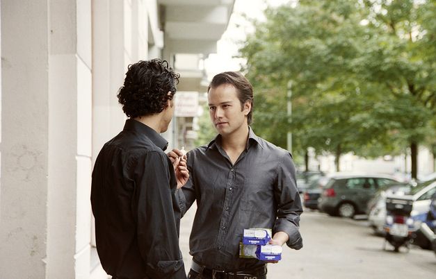 Still from the film "Fremd. Yaban." by Hakan Savaş Mican. Two young men on a street looking at each other. 