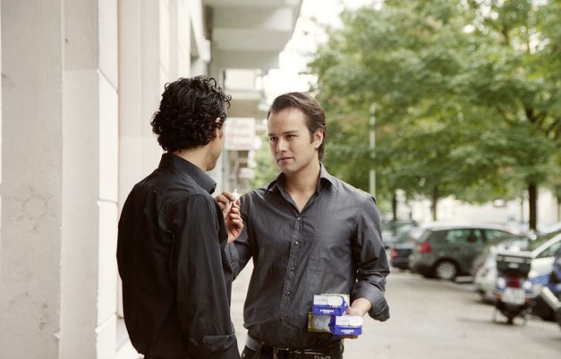  Filmstill aus "FREMD. YABAN." von Hakan Savaş Mican. Zwei junge Männer stehen auf der Straße und wenden sich einander zu. 