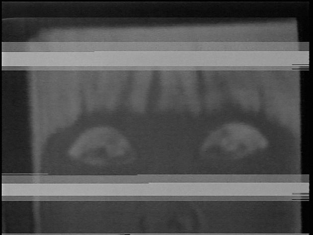 Still aus „Blinking“ von Takahiko Iimura: ein schwarz-weißes Videobild, mit Störungen, auf dem etwas zu erkennen scheint, was zwei Augen mit Wimpern sein könnten.